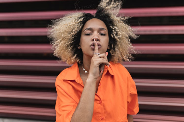 Young woman using the quiet sign before revealing Scorpio's ruling planet.
