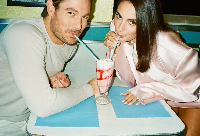 Two people smiling while sharing a milkshake with two straws at a diner table with a blue and white ...