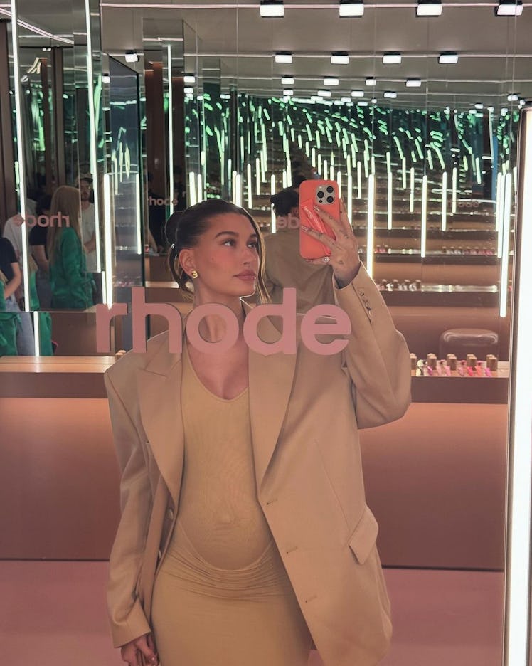 Woman in beige outfit taking a selfie in a mirror-lined room with neon lighting.