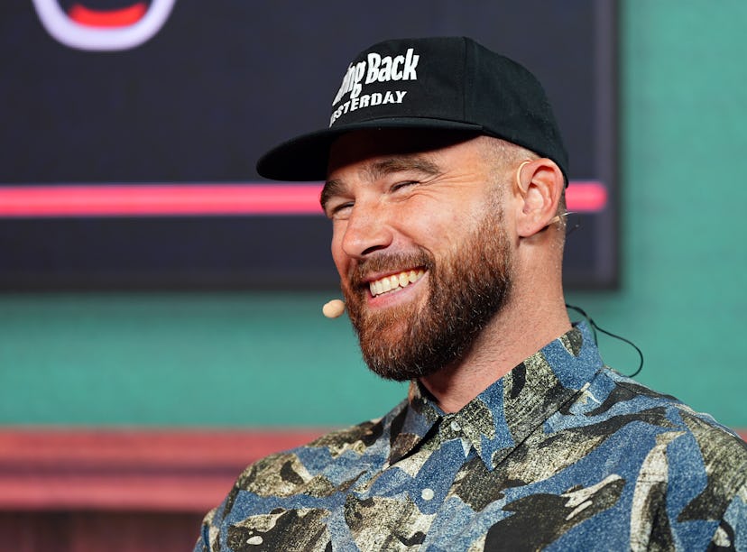Man with beard laughing, wearing a camo shirt and black cap that says "JumpBack Yesterday." He is ou...
